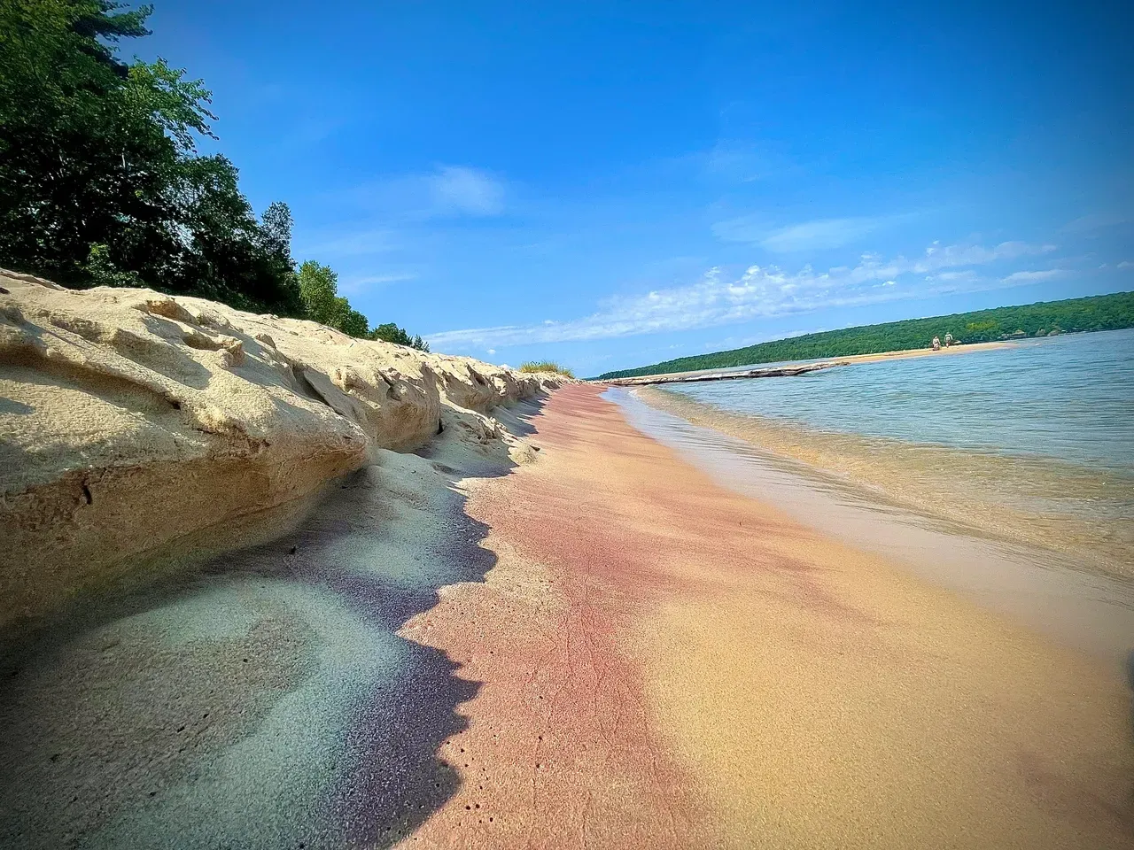 Hardened Sand dunes from being wet and then dry that are lined with trees that eventually slant down and form into a smooth beach with the clear waters of Lake Superior washing ashore. 