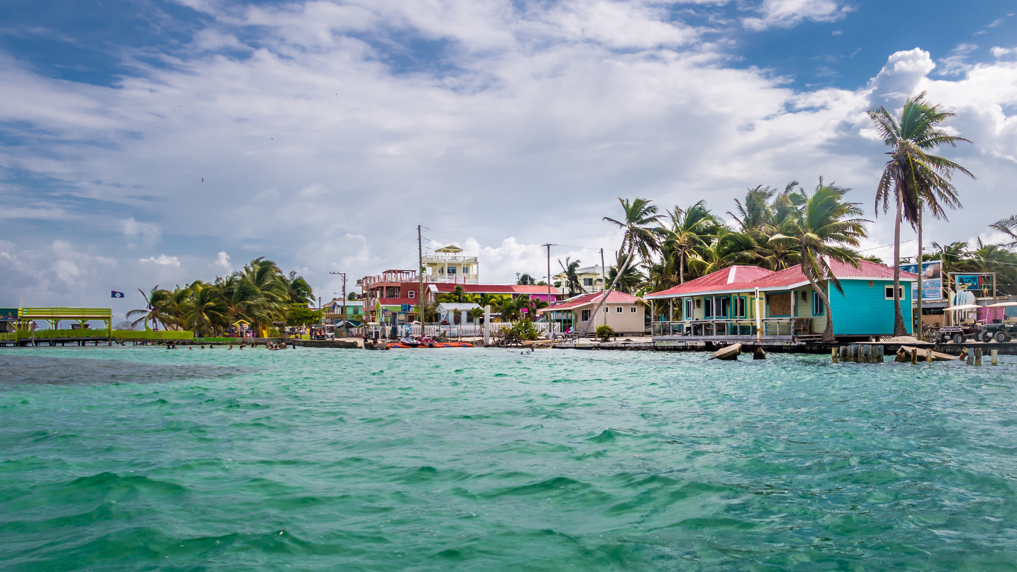 Colorful buildings in the beachside town of Caye Caulker, Belize with palm trees blowing and clear caribbean waters