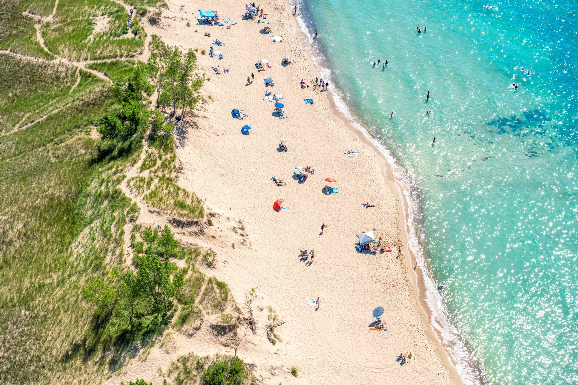 Ariel view showing people playing on a beach with crystal clear blue waters on Lake Michigan's Oval Beach.