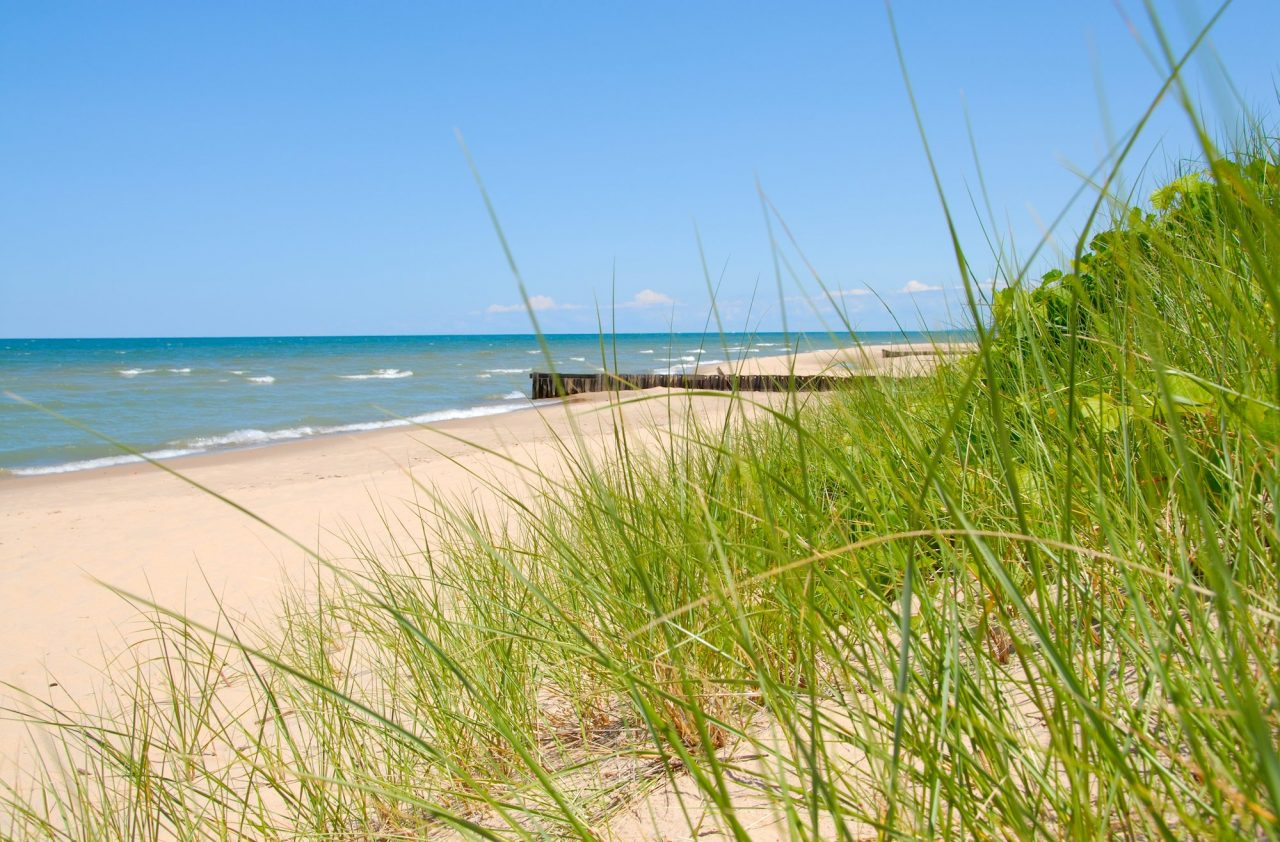 small waves on a lake leading to a sandy beach that then has a grassy dune leading up to the beach.