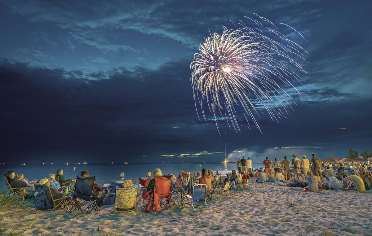 Bunch of people gathered sitting on the beach at night in chairs watching fireworks for 4th of July at Manistee’s First Street Beach.