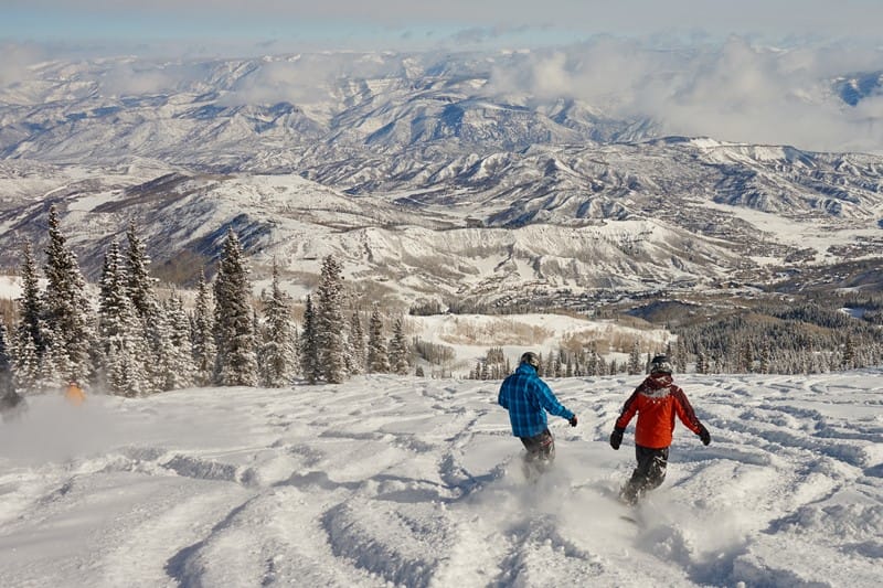 Two people snowboarding down a fresh bit of fallen powder at Aspen Snowmass Resort.