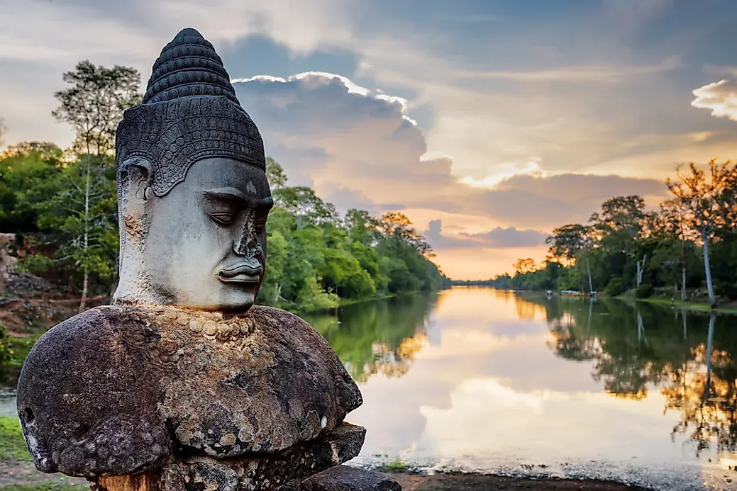 Ancient statue with a river behind in and the sun setting in Cambodia.