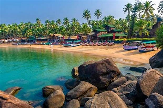 Beach resort with emerald, green calm ocean waters with palm trees in Goa India.