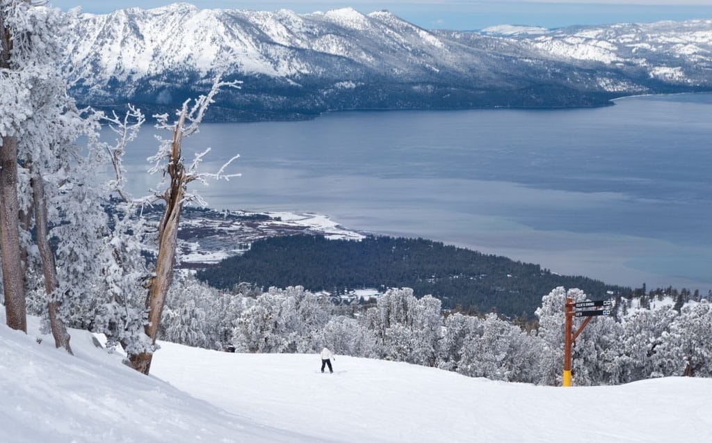 Ski run showing a person on a snowboard with a view of Lake Tahoe in front of them offering an incredible view like you won't see anywhere else. 