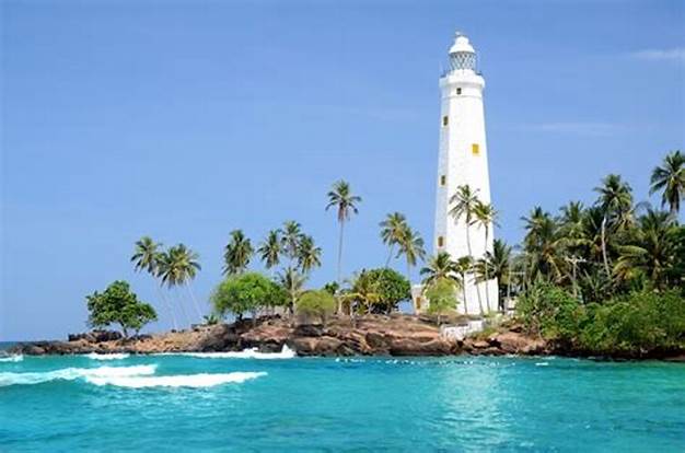 A lighthouse surrounded by palm trees next to the oceans edge in Sri Lanka.