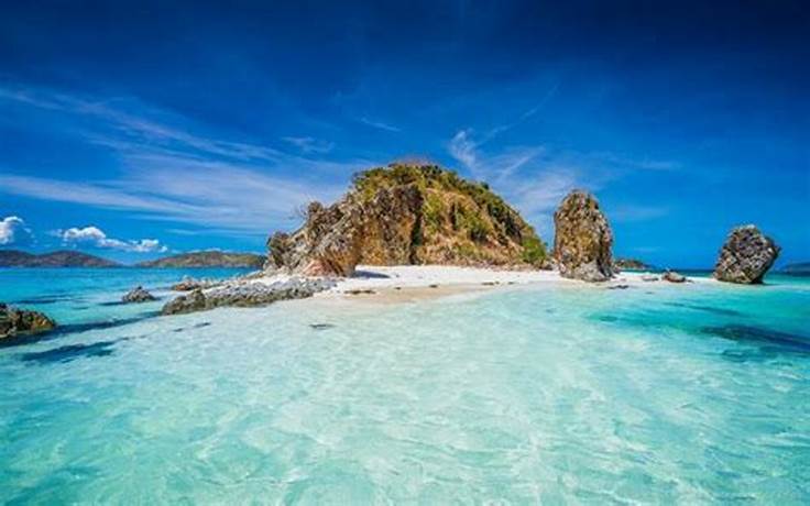 Clear blue ocean water with a tiny rock island that has white clean sand in the Philippines.