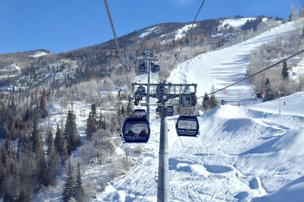 The new gondola at Steamboat Springs Ski Resort with people riding up the mountain and ski runs shown below with ski tracks in the snow from recent skiers. 