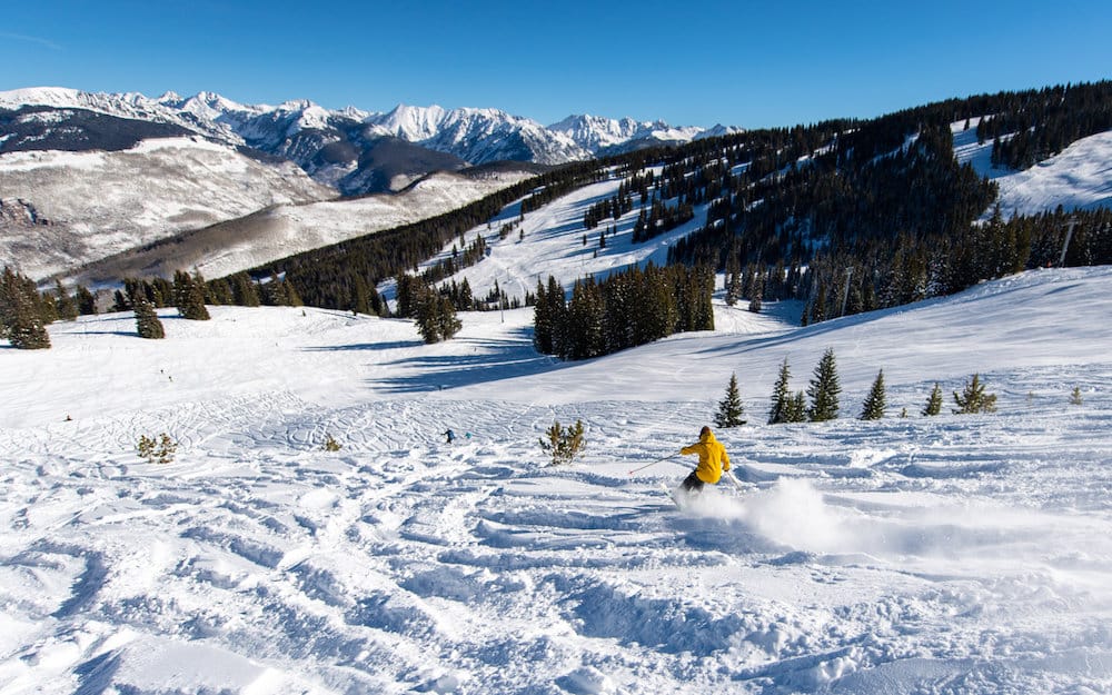 Man skiing down powdery run at Vail Ski Resort with clear skies and a beautiful view of the mountains.