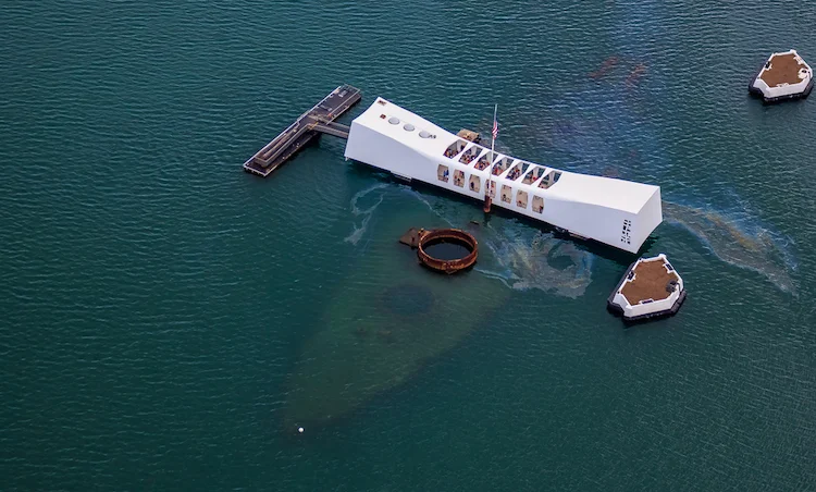 Ariel view of a white building that is on top of the water that is over the wreckage of a sunken ship.