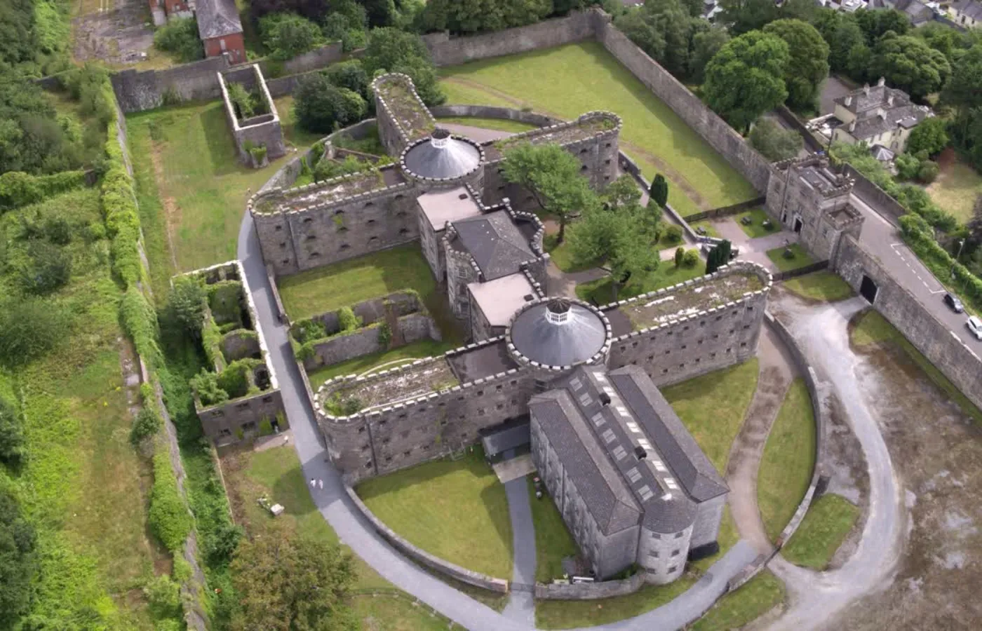 Ariel view of a 19th century prison that in the shape of two plus signs stacked on top of each other and surrounded by lush green grass that is typical of Ireland. 