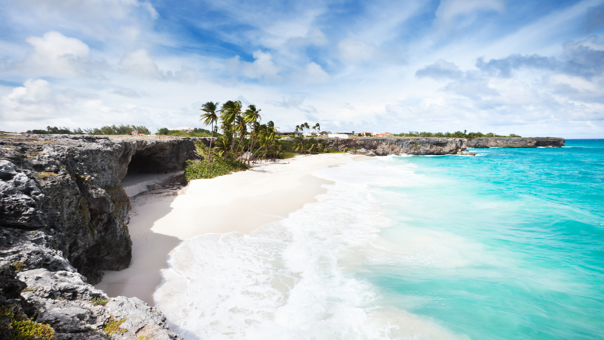 Cliff leading down to a pretty white sand beach that has bright clear blue Caribbean waters. 