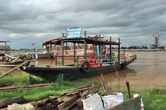 Old boat on a large muddy river with the boat pulled up on the river bank on a path of grass. 