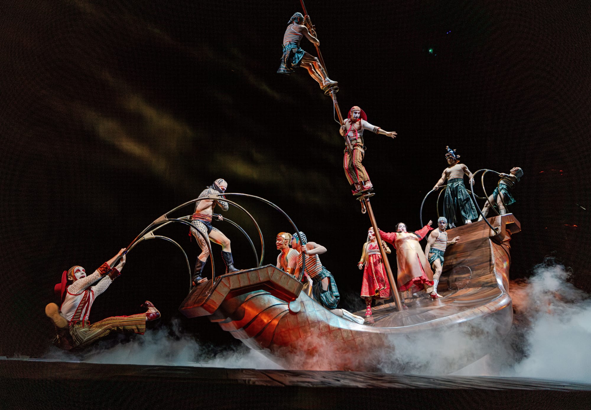 Las Vegas Cirque du Soleil performers doing a balancing act on a wooden boat with one handing off the front and two hanging from the mast of the ship. 