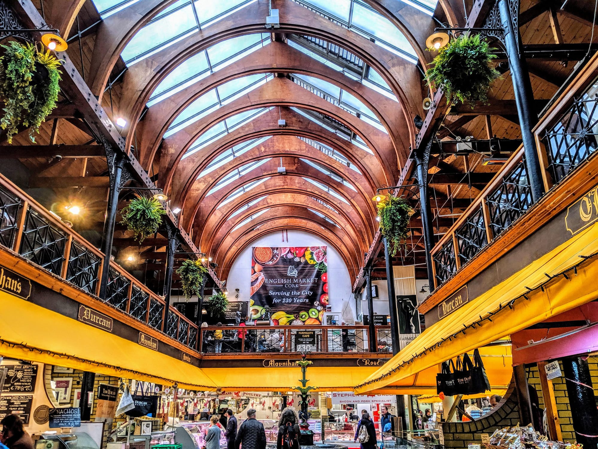 Two level market with food vendors selling produce and other goods to shoppers. 