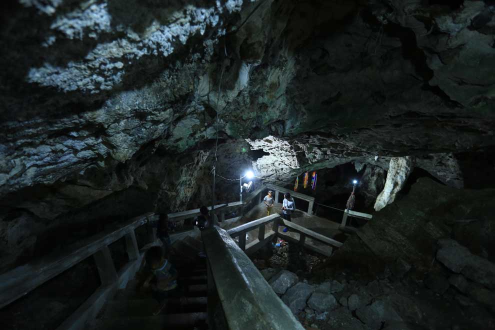 Stairway down into a large cave with people down at the bottom of the stair near a light. 