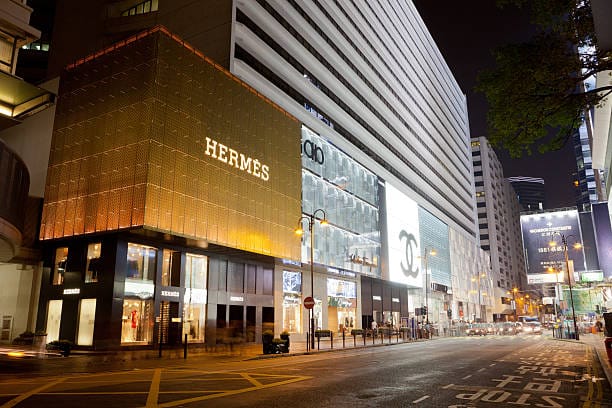 Hermes store front with golden color painted on the building and a sign lit up with the businesses name on a street in Hong Kong. 