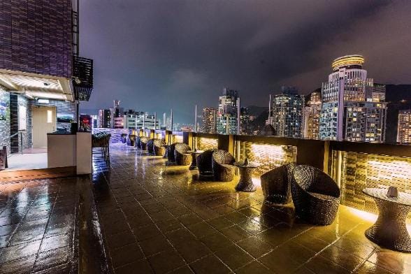 Patio of a high end hotel in the Admiralty area of Hong Kong at night with table and chairs lining the sidewalk outside the front door. 