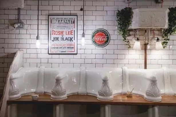 A quirky café in Fitzrovia, London, featuring a seating area made from repurposed Victorian urinals against a white-tiled wall.