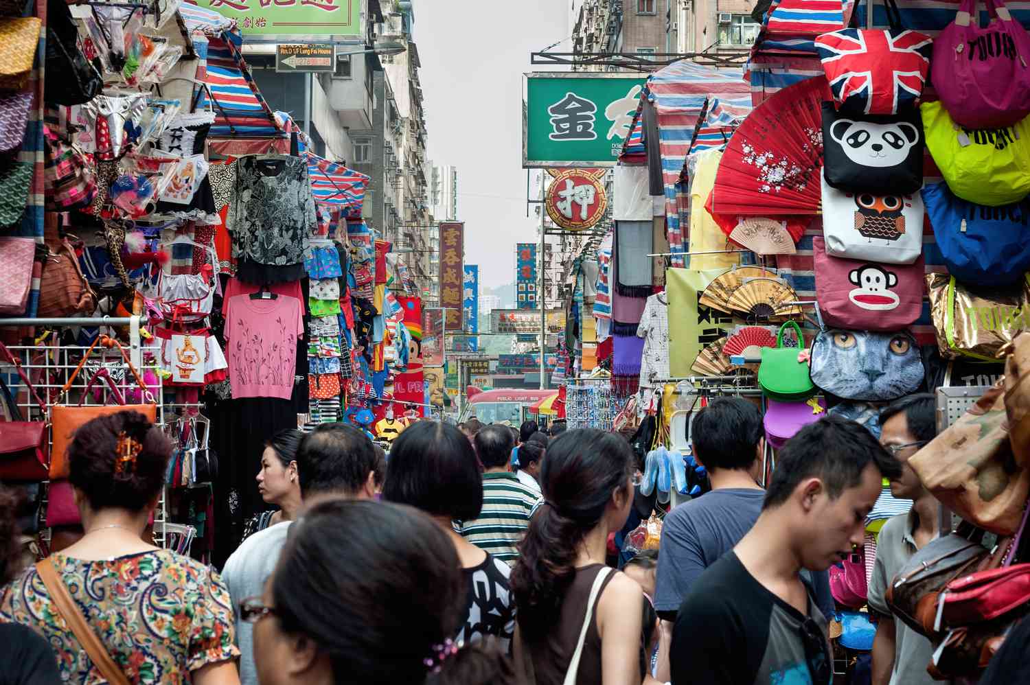 People walking narrow market street packed with shops and people selling all types of cheap goods. 