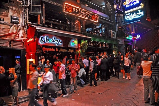 Lots of people outside drinking on a streets lined with pubs are night time.