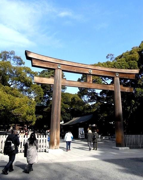 Japanese style entrance to Meiji Shrine with people walking in and out.