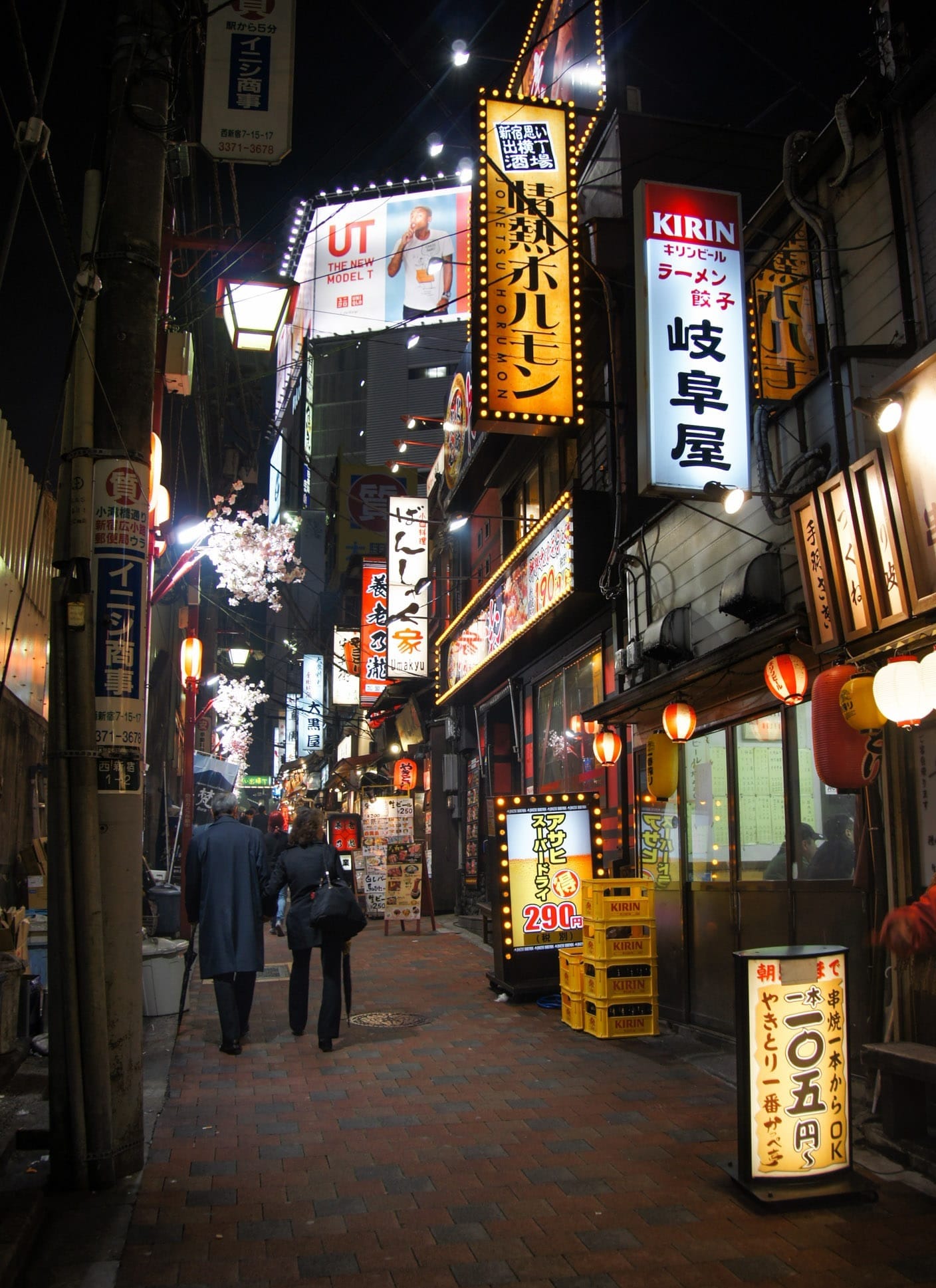 People walking the Omoide Yokocho area of Tokyo at night, where the street in red brick and lined with places to eat. 