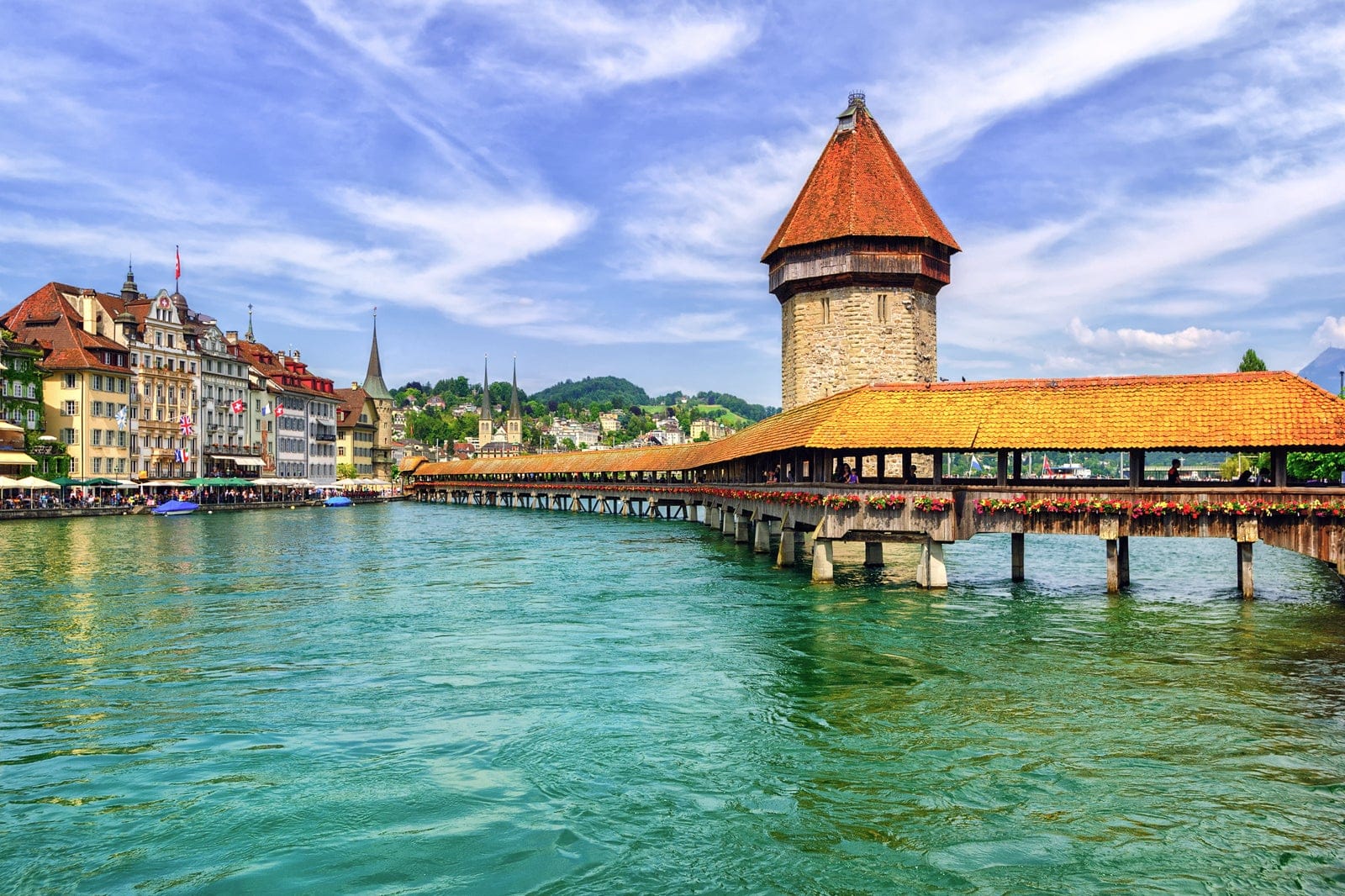 At edge of the city of Lucerne, Switzerland, A covered pier with brown shingles going out into the water of Lake Lucerne.