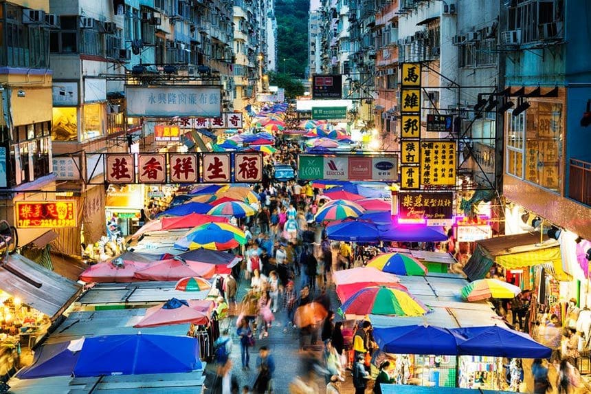 Vendors with tents set up selling their goods and services on a busy market street at night. 