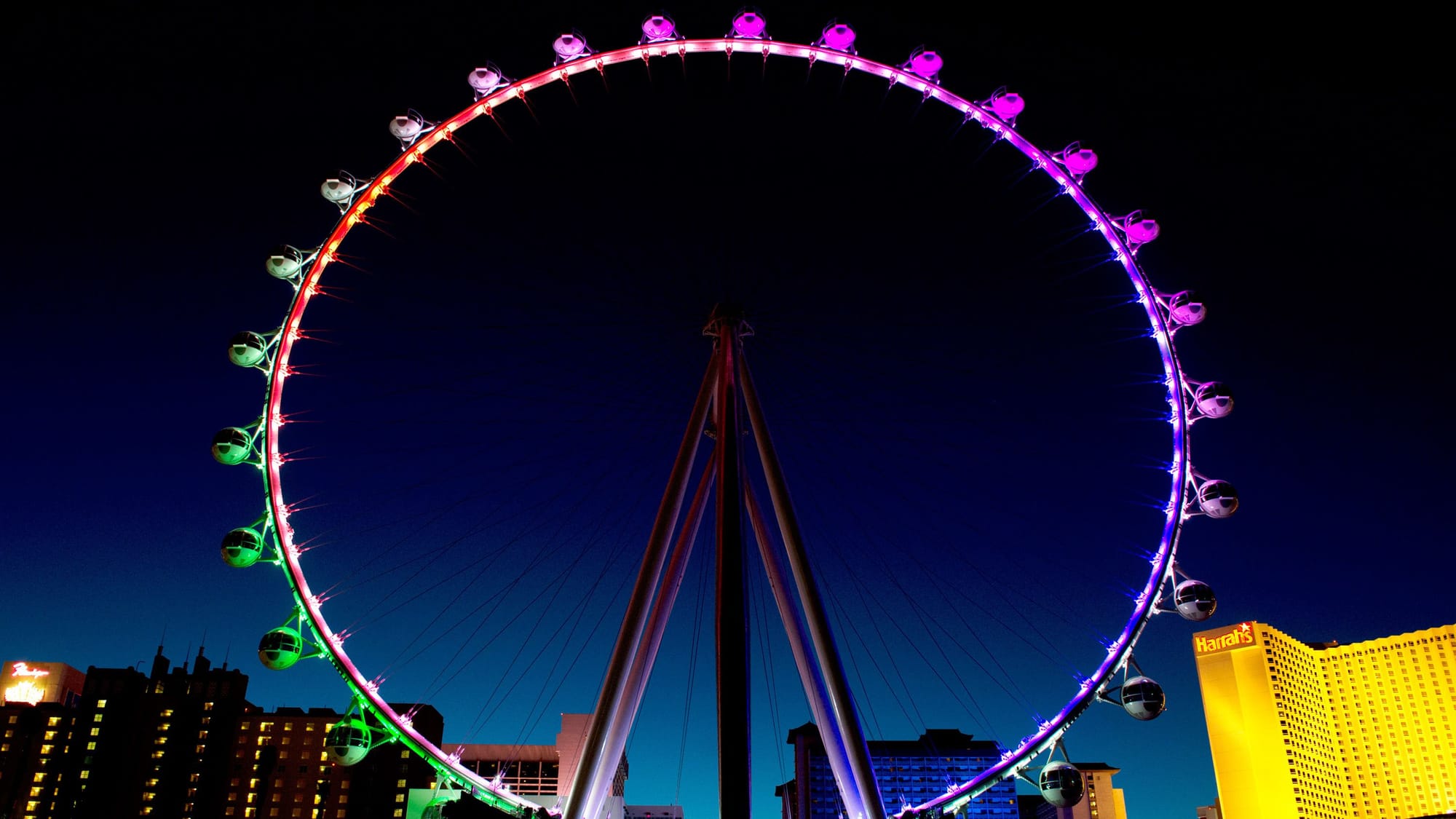 Ferris wheel lit up in green and purple with casinos in the background at night in Las Vegas.