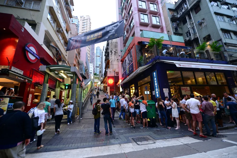 People standing outside on the patios and streets socializing at bars and places to eat.  