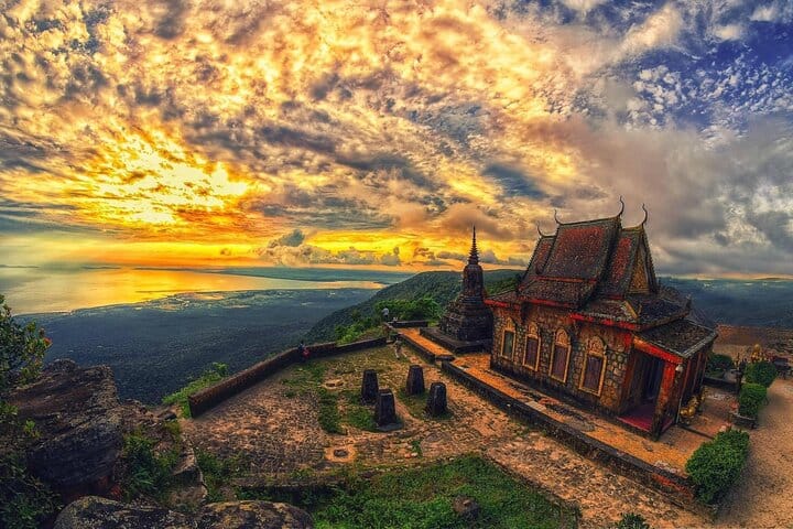 A old stone looking building that is well maintained on a cliff side overlooking the ocean at sunset. 