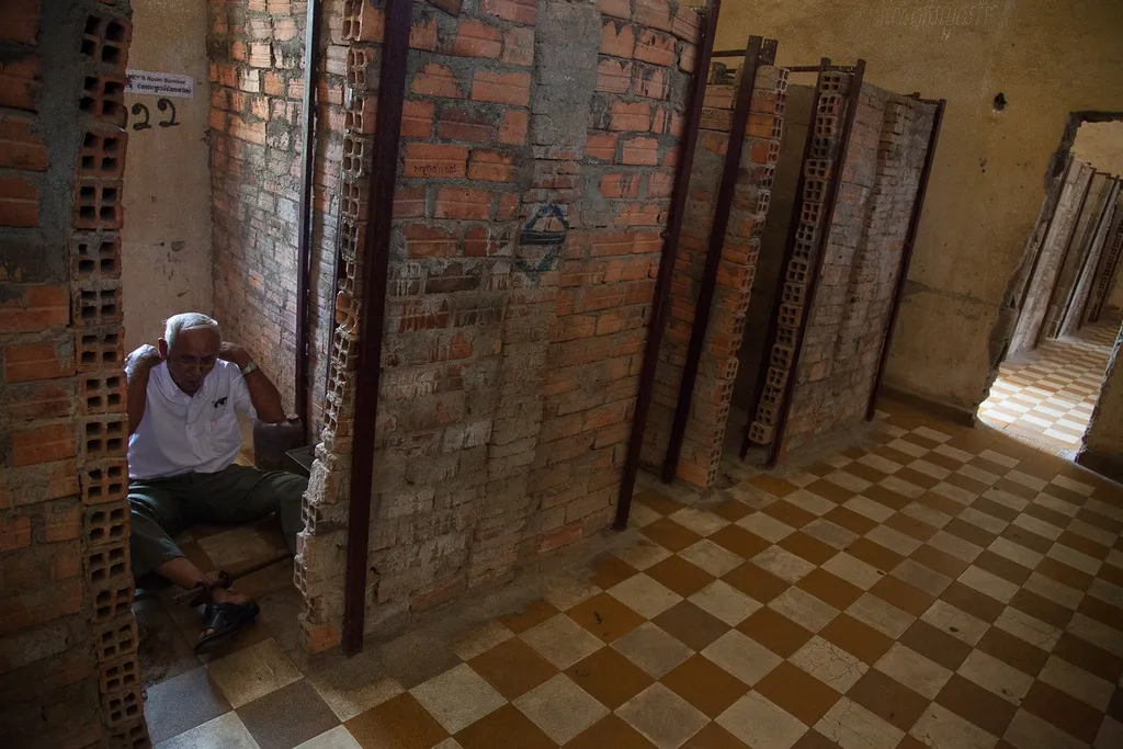 Man sitting inside what use to be a prison cell with walls made of brick at  the Killing Fields and Tuol Sleng Genocide Museum in  Phnom Penh.