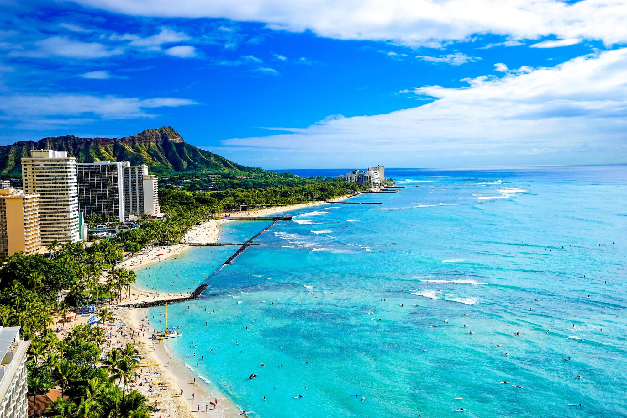 Ariel views of a beautiful beach and clear blue waters, with the beach being lined with towering resorts.