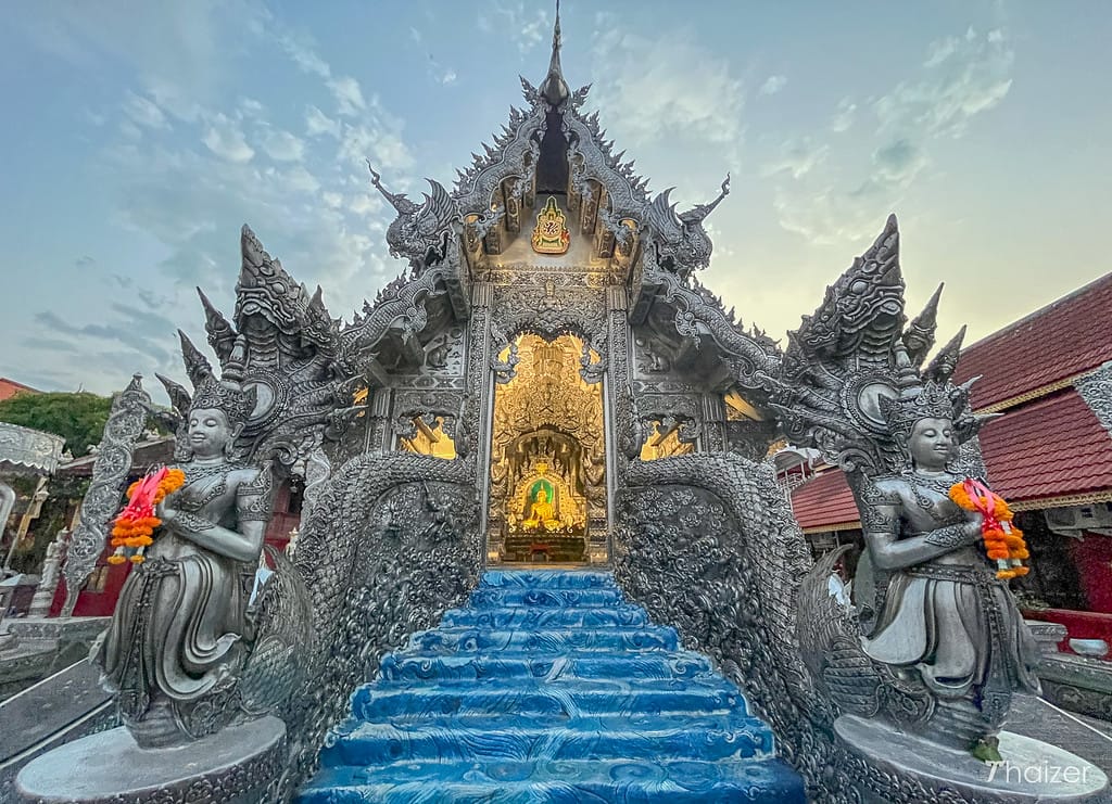 Silver temple with golden door that appears to be covered in reptile scales and Buddist statues on each side of the entrance that that is a bright metallic blue color