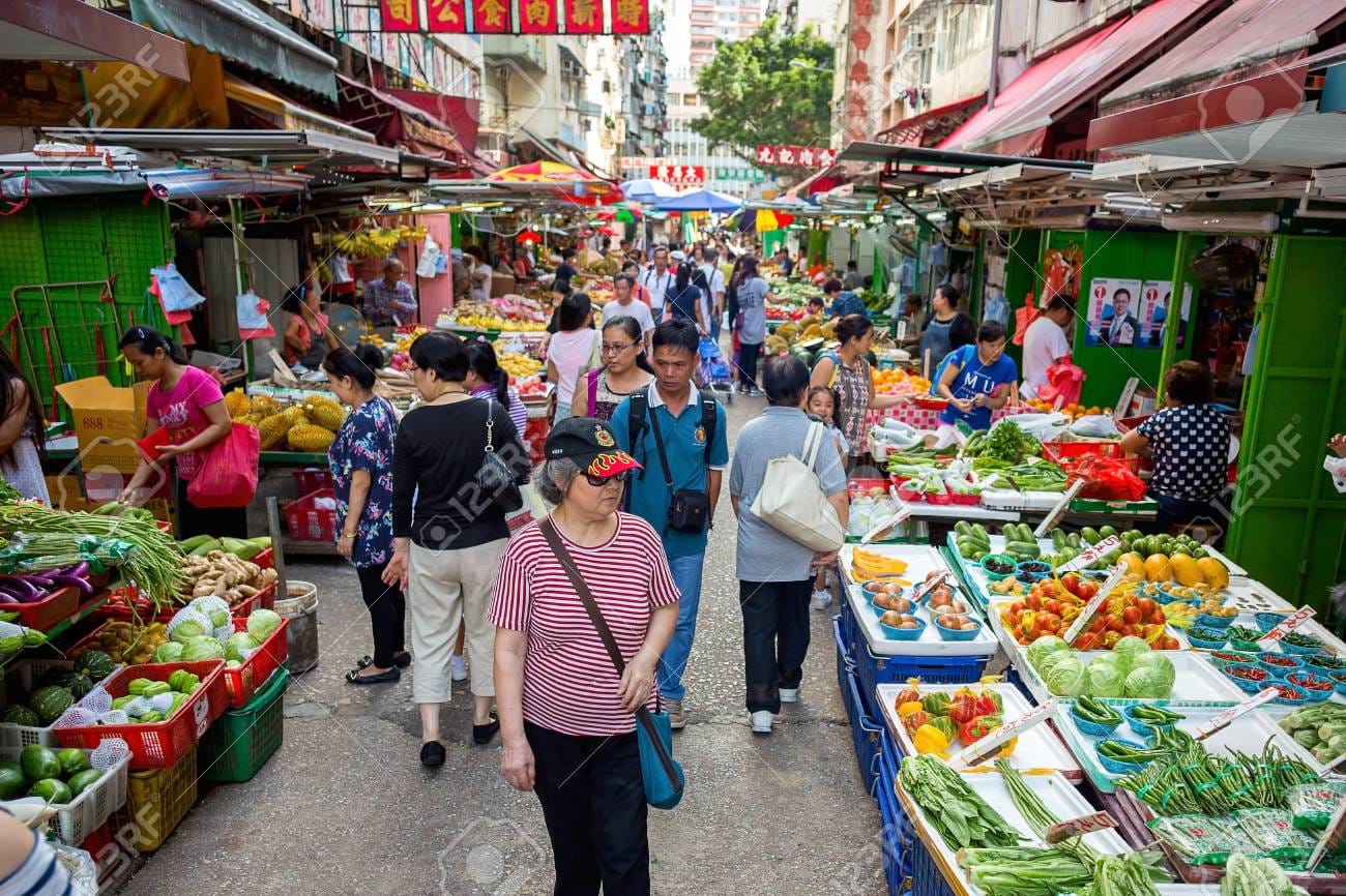 People walking and shopping for fresh produce from a local market with lots of vendors selling freshly picked veggies. 