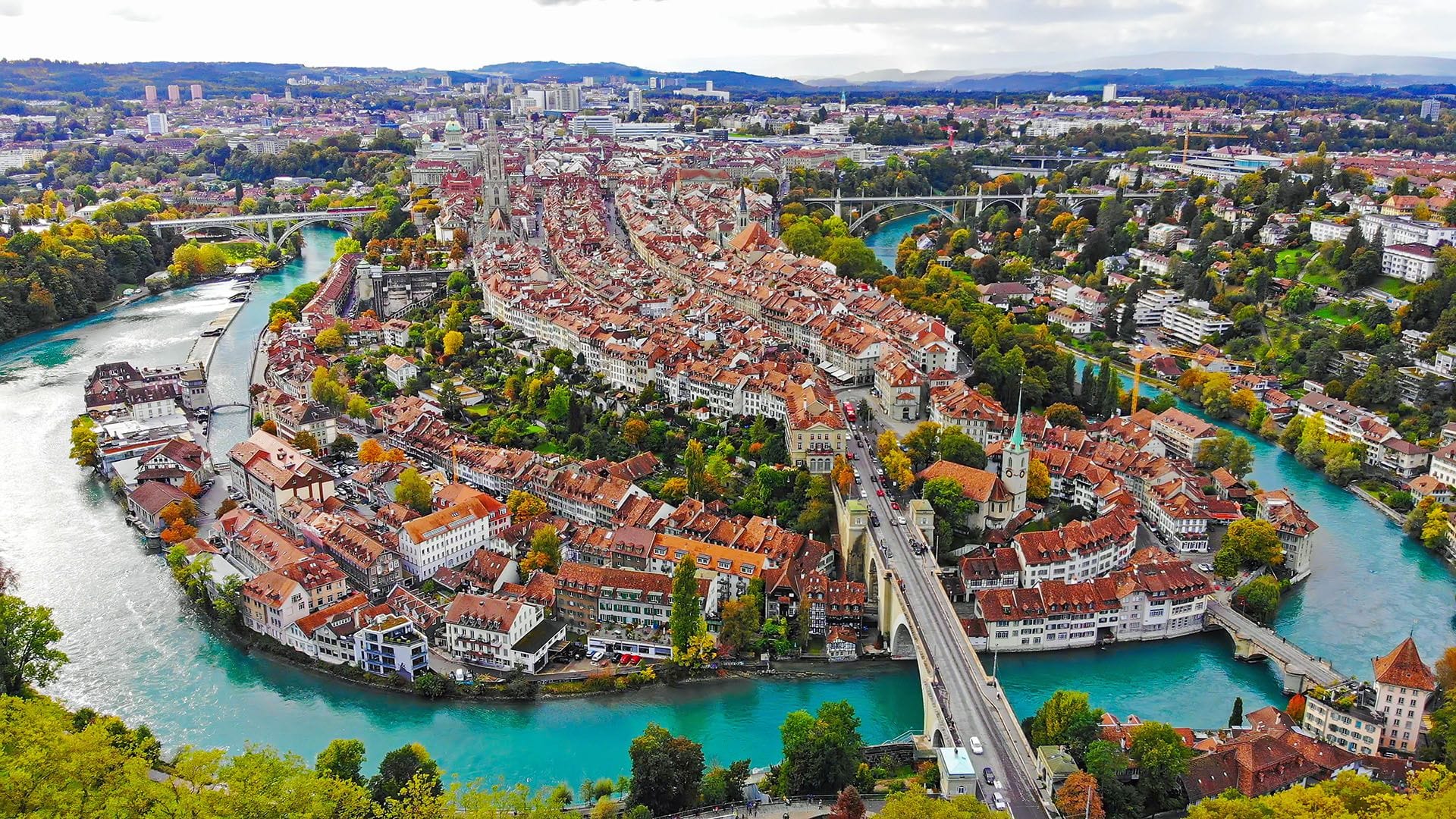  Aerial view of Bern, Switzerland, showcasing the historic Old Town, the Aare River, red-roofed buildings, and scenic bridges.