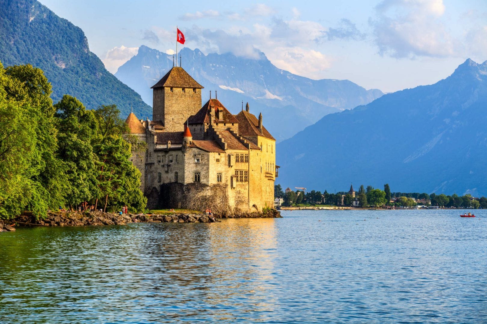 And old castle or manor on he edge of Lake Geneva, Switzerland with large cloudy mountains in the background.