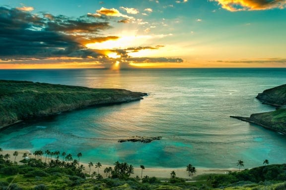 A beach almost enclosed by land in the shape of a horseshoe with the sun setting out at sea. 