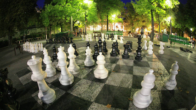 A large chess board has been painted onto the parks concrete with large 2 to 3 foot chess pieces for people to play chess on a giant chess board in Parc des Bastions in Geneva, Switzerland.