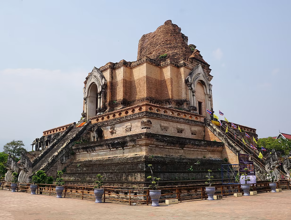 Ancient temple with a large square base with stairs going up on each of it's 4 sides, and part of the temple has eroded away from age. 