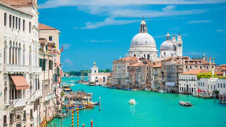 the grand canal in Venice, Italy with the sun shining and showing the emerald waters and seaside buildings