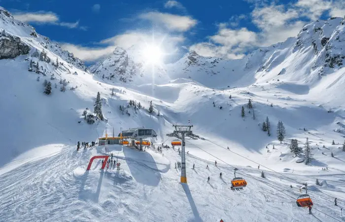 Jagged peaks of mountains covered in snow with a chair lift taking skiers to the top on a sunny day.